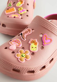 Zoccoli rosa con variomodi ciondoli in plastica colorata, tra cui un fungo, un'ananas, un cuore, un fiore e un arcobaleno. Progettati con fori di ventilazione.