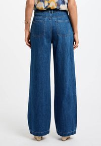 Løse blå denimjeans med høy midje og to baklommer. Stoffet har en glatt tekstur og et klassisk femlomdesign.