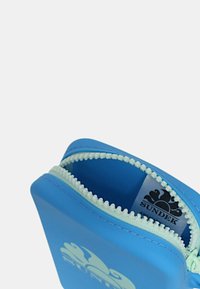 Pochette blu in silicone con zip bianca e marchio all'interno. Design compatto, texture liscia, con logo sul fronte.