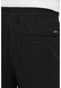 Pantalons noirs à taille élastique avec une poche arrière, fabriqués à partir d'un tissu léger et texturé. Comprend une petite étiquette cousue sur le côté.