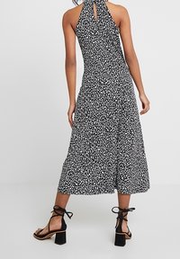 Black and white halter-neck dress with leopard print, flowing midi length, and a keyhole back detail; paired with ankle-strap block-heel sandals.