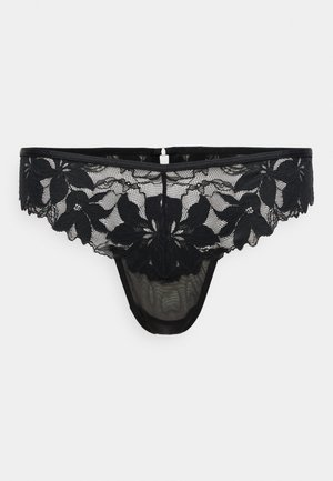 Tanga de encaje negro con un patrón floral, malla transparente y borde festoneado, acabado con un pequeño cierre en la parte trasera.