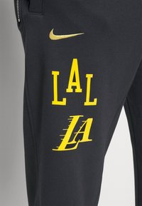 Sorte sweatpants med gule "LAL" og "LA" grafiktrykker. Teksten fremhævet med en bevægelseseffekt; inkluderer et lille gul Nike-logo.
