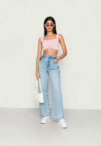 Top cropped rosa claro com detalhes franzidos e laço na frente, combinado com jeans de perna larga azul claro de cintura alta e ténis brancos. Bolsa branca.