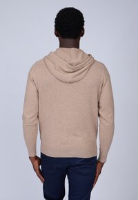Sweat à capuche tricoté beige, avec un capuchon à cordon de serrage, des manches longues et une coupe décontractée. Texture lisse, tissu doux et coutures minimales.