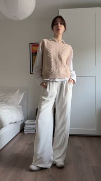 Gaiši rozā adīts veste ar teksturētu rakstu, pār sārtiem baltu kreklu, kopā ar baltām, vaļīgām biksēm. Vienkārša apavi noslēdz izskatu.