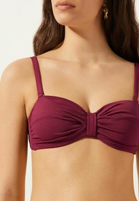 Haut de bikini texturé mauve avec un détail de nœud torsadé au centre et des fines bretelles ajustables. Finition en tissu lisse.