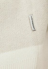 Lys beige strikket sweater med et tekstureret mønster, der har en ribbet kant og et lille mærke med "ORIGINALS™" logo.