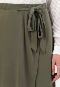 Jupe vert olive en tissu doux avec un détail de taille nouée, présentant une texture lisse et un design drapé.