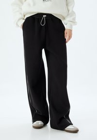 Zwarte sweatpants met een wijd model, elastische tailleband en verstelbare koordsluiting. Bevat witte zijstreep en een zachte stoftextuur.