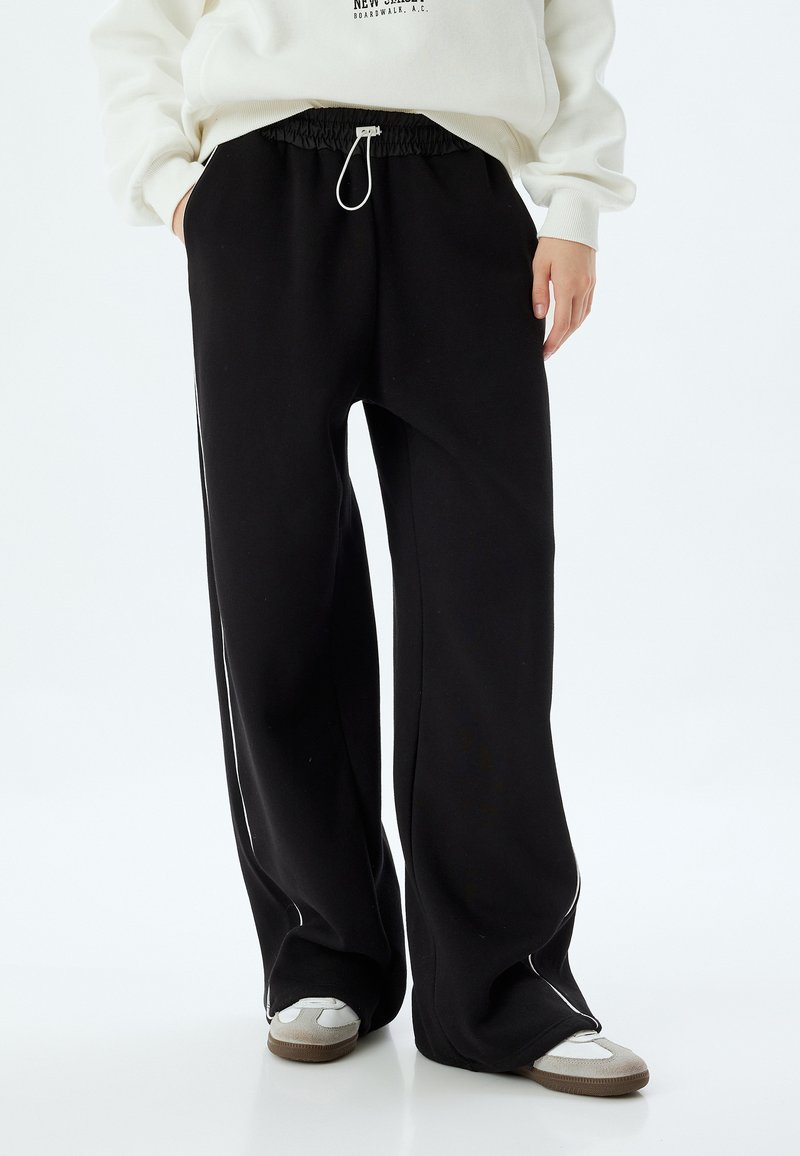 Zwarte sweatpants met een wijd model, elastische tailleband en verstelbare koordsluiting. Bevat witte zijstreep en een zachte stoftextuur.