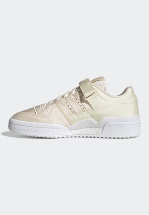Low-top beige sneaker with laces, a Velcro strap, perforated side stripes, and thick white sole on a plain background.