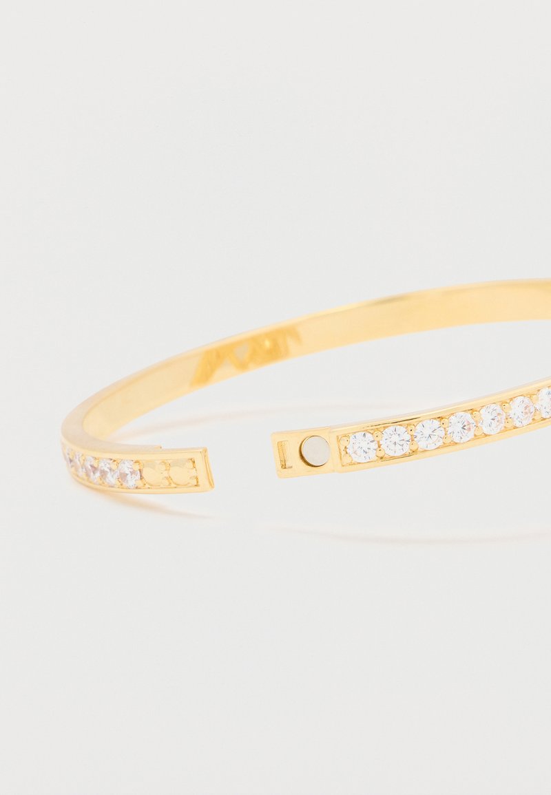 Gold cuff bracelet featuring a glittering line of clear crystals along one edge, with an open design and smooth metallic finish.