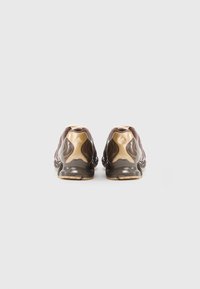 Calçado com parte superior em malha castanha com detalhes dourados brilhantes, calcanhar de plástico castanho liso e sola texturada para aderência.