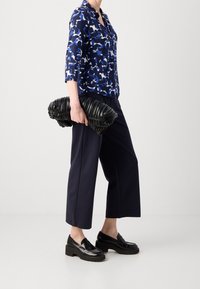 Camisa azul de estampado con mangas de tres cuartos, pantalones de pierna ancha en color marino y un clutch negro con frunces, combinado con mocasines negros de plataforma.