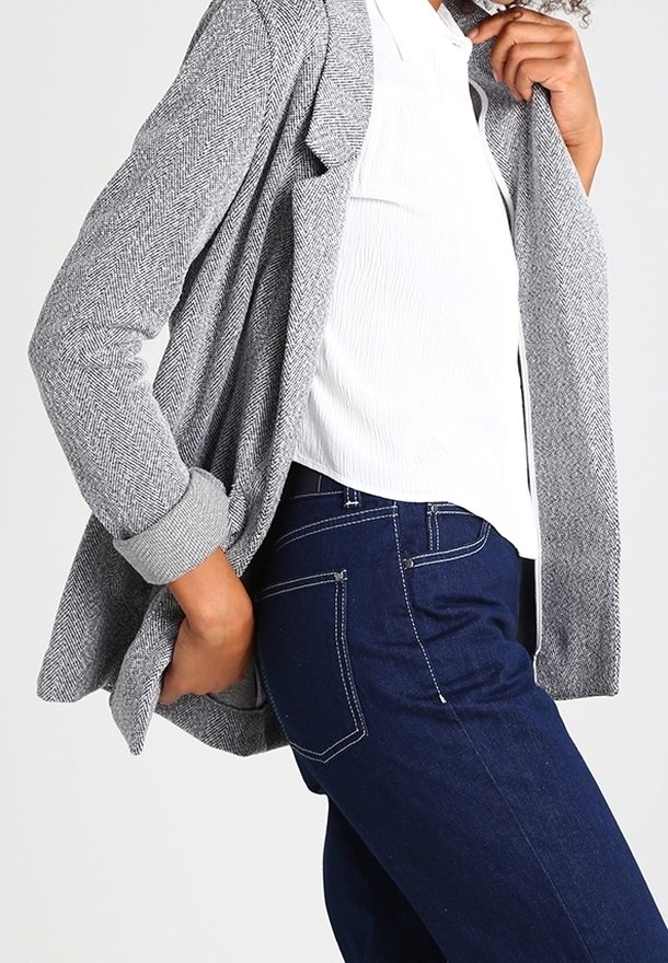 Šedý herringbone cardigan s volným střihem a ohrnutými rukávy, vrstvený přes bílou košili, spárovaný s tmavě modrými slim-fit džíny.