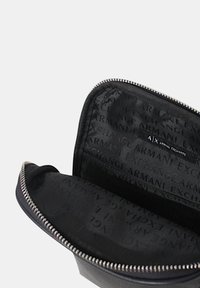 Portafoglio in pelle nera con chiusura a zip. L'interno presenta una fodera in tessuto testurizzato con il logo "Armani Exchange" in un motivo ripetuto.