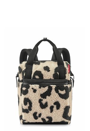 Square-shaped backpack with beige and black leopard print fuzzy fabric, black straps, a front zipper pocket, and a red logo tag on the side.