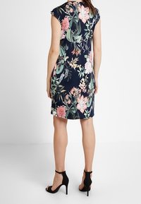 Kwiatowa sukienka na granatowym tle, z krótkimi rękawami i dopasowaną sylwetką. Posiada różowe i białe kwiaty, połączona z czarnymi szpilkami.