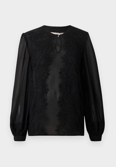 Melna blūze ar garām caurspīdīgām piedurknēm; tajā ir sarežģīta mežģīņu apdare priekšpusē un neliela atslēgas caurums kakla rajonā.