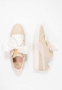 Baskets synthétiques beiges avec des accents roses, dotées de larges lacets en satin blanc et de semelles en caoutchouc texturé. Doublure intérieure à motif visible.