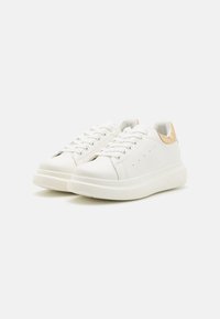 Hvite lær sneakers med teksturert overflate, rund tå og en kremfarget gummisåle, med en lys brun aksent ved hælen.