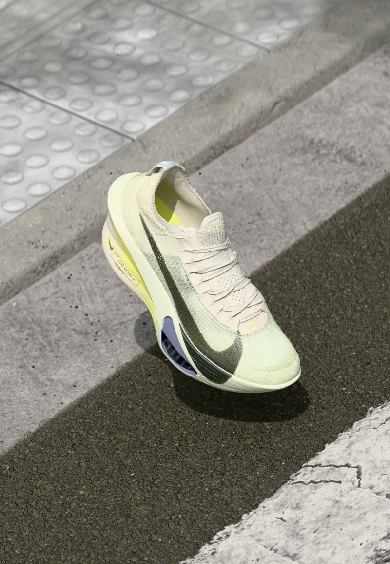 Atletische schoen met een lichtgele mesh bovenwerk, getextureerde accenten, een groene en zwarte swoosh, en een uniek blauw zoolontwerp.