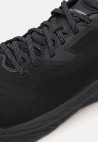 Černá atletická bota s texturovaným textilním svrškem, síťovanými sekcemi a syntetickými akcenty. Šňůrky a gumová podrážka jsou také černé.