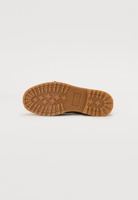 Semelle de bottes en caoutchouc marron avec une surface texturée, présentant de profonds crans et une zone de marquage rectangulaire près du talon.