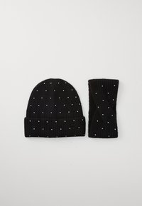 Set di berretto lavorato a maglia nero e polsini con una texture a coste e macchie bianche sparse. Il berretto ha un risvolto e una parte superiore arrotondata.