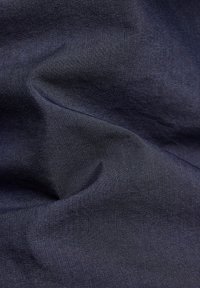 Tmavě modrá látka s hladkou texturou, která má jemný lesk a tkaný vzor, uspořádaná tak, aby ukázala hloubku a přirozen é záhyby.