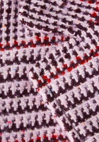 Textiel met een rood, wit en zwart geruit patroon, voorzien van gestructureerde, fuzzy vezels en multicolore spikkels overal.