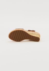 Brown espadrille sandal with a woven jute upper, textured rubber sole, and adjustable strap for secure fit. Features logo detail on sole.