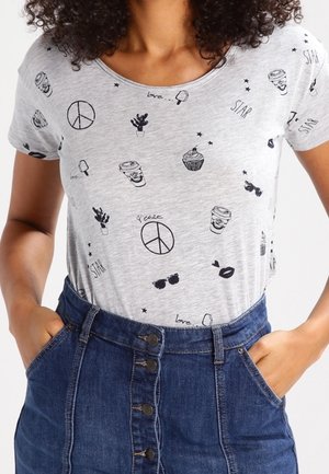 Femme portant un t-shirt gris clair avec des gribouillis noirs (symbole de paix, tasses à café, cupcake, lunettes de soleil) rentré dans une jupe en jean taille haute boutonnée.