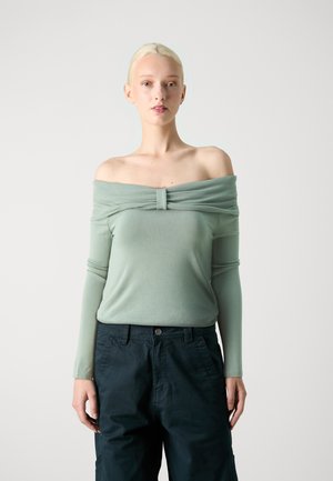 Top verde claro de hombros descubiertos con tejido gathered en el escote, combinado con pantalones cargo oscuros y holgados. Textura suave.