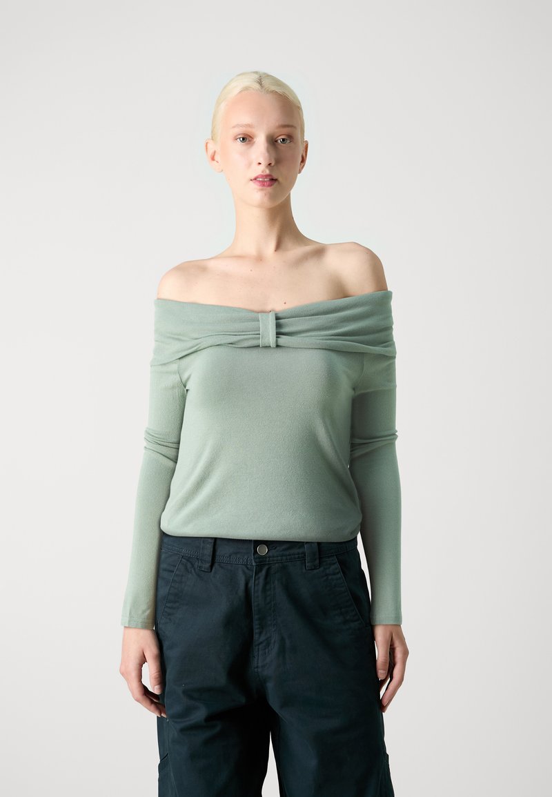 Off-shoulder lysegrønn topp med samlet stoff ved halsen, sammen med mørke, vide cargo-bukser. Glatt tekstur.