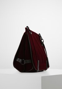 Bolso de terciopelo burdeos con acentos de cuero negro, con diseño plegable y anillos para correas ajustables. Acabado texturizado y forma semiestructurada.