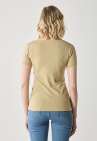 Lys beige tettskjorte med korte ermer, jevn tekstur, rund hals, kombinert med blå denim jeans med baklommer.
