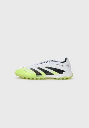 Crampons de football blancs et noirs avec des accents verts vifs, tige synthétique texturée, lacets et semelle en caoutchouc moulé avec des crampons antidérapants.