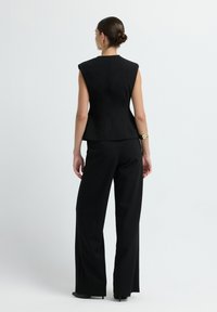 Top senza maniche di colore nero, con scollatura alta, abbinato a pantaloni larghi a vita alta, caratterizzati da una texture liscia e dettagli minimi.
