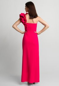 Długa, dopasowana sukienka wieczorowa w intensywnym różu, z pojedynczym falbaniastym ramieniem i zapięciem na suwak z tyłu. Gładki materiał oraz elegancka sylwetka.