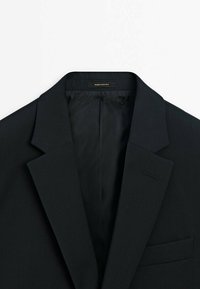 Zwarte blazer met notch-lapels, enkele borstzak en een gladde binnenvoering. Gemaakt van lichte stof, met subtiele stikdetails.