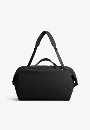 Schwarze Reisetasche mit gepolstertem, verstellbarem Schultergurt und zwei Tragegriffen, vor weißem Hintergrund.