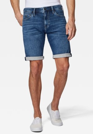 Shorts en denim de couleur bleu foncé, avec un ourlet roulé, un design classique à cinq poches et une fermeture à boutons. Associés à des baskets blanches.