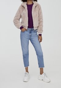 Faux fur beige jakke med høj krave, parret med en lilla ribbet sweater og lyseblå tapered jeans. Hvide chunky sneakers fuldender looket.