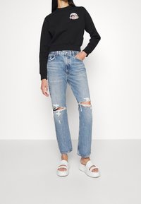 Sudadera corta negra con un diseño gráfico, combinada con jeans desgastados de color azul claro con detalles rasgados y sandalias de plataforma blancas.