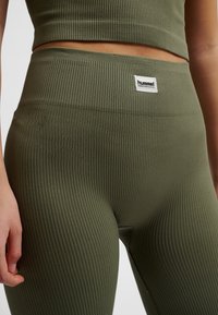 Olivgröna ribbade leggings med hög midja och en liten vit märkesetikett, med ett texturerat tyg och figurnära design.