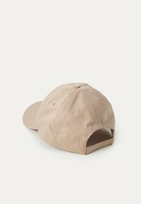 Beige baseball cap med tekstur i stoffet, rund krone, buet skygge og justerbar rem bagpå. Har ventilationshuller og syningsdetaljer.