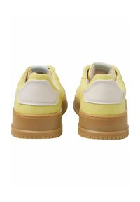 Baskets en daim jaune avec un accent en cuir crème sur le talon. Présentent une semelle en caoutchouc texturée et une languette rembourrée pour plus de confort.