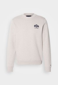 Lys grå sweatshirt med lange ærmer og rund hals. Har et marineblåt broderet logo på brystet. Blød tekstur og ribbede manchetter.